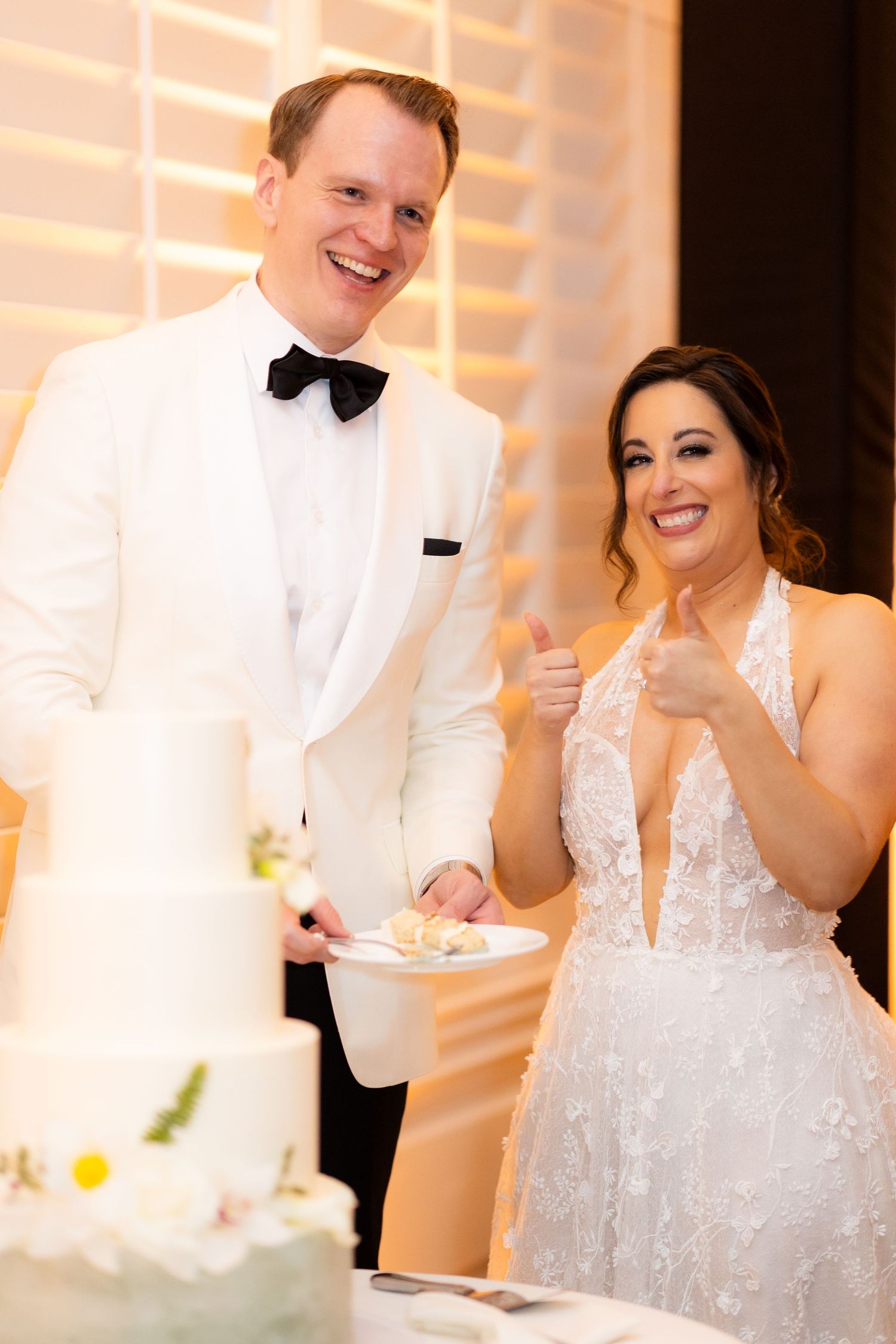 Newlyweds share a joyful moment cutting their elegant white wedding cake together at the reception.