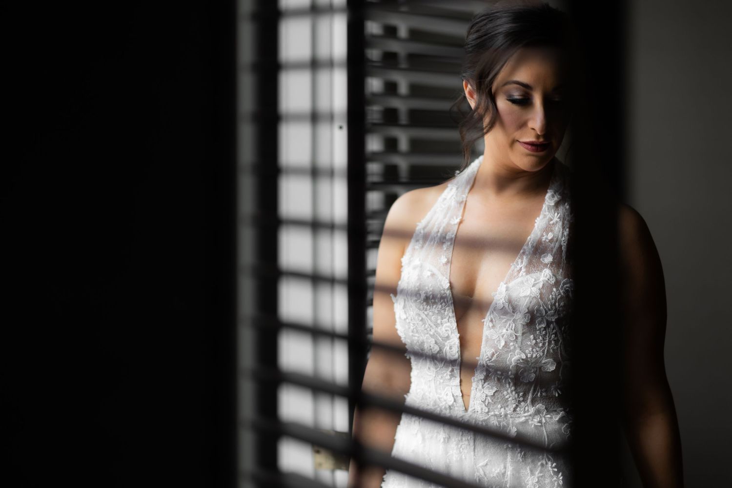 Artistic bridal portrait with dramatic window lighting highlighting a white lace wedding dress.