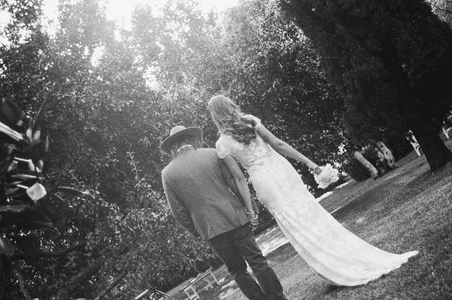 Black and white photo of a bride and groom dancing outdoors surrounded by lush green trees at a wedding.