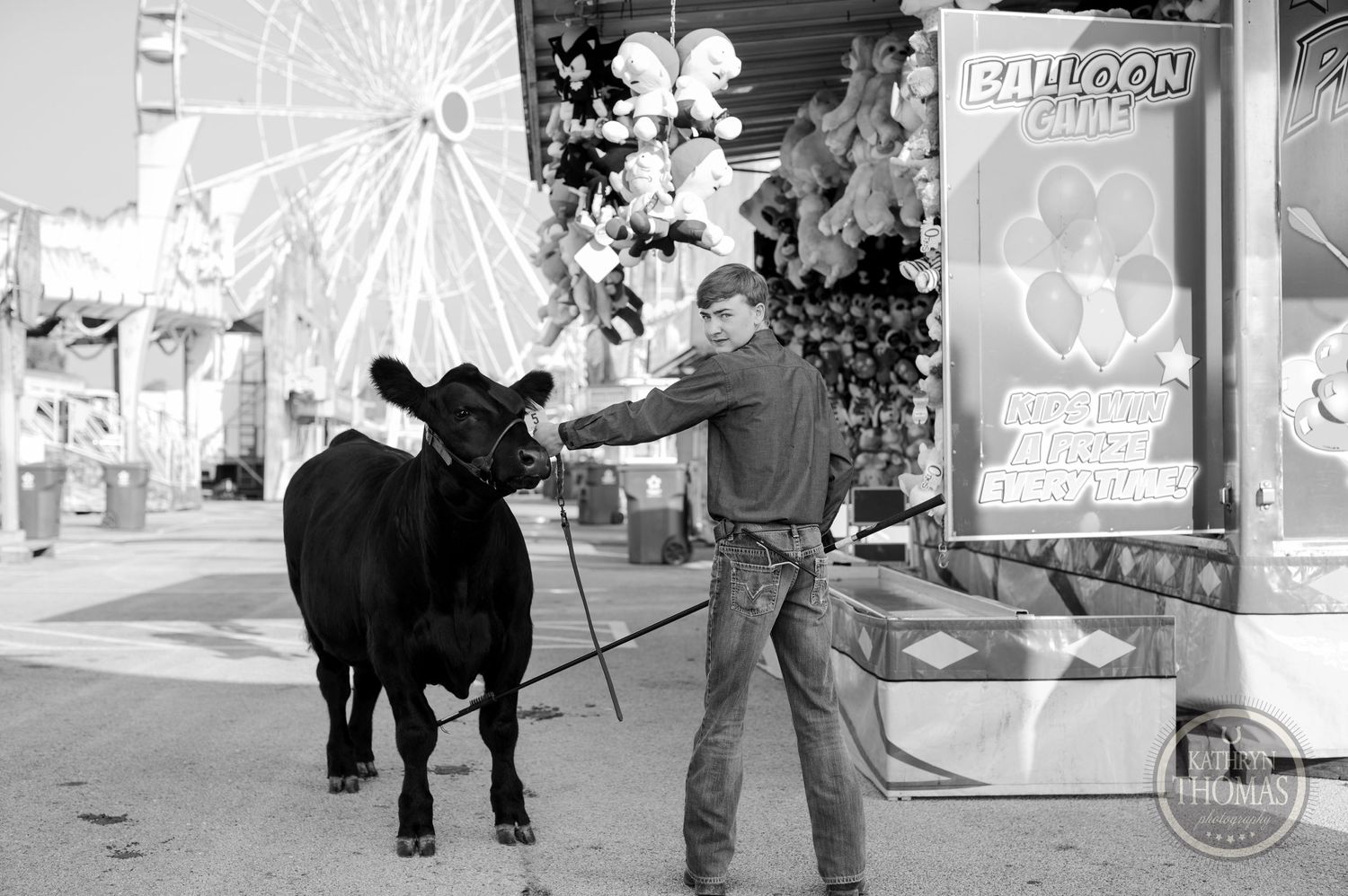A black show animal stands with handler near carnival game booths and ferris wheel.