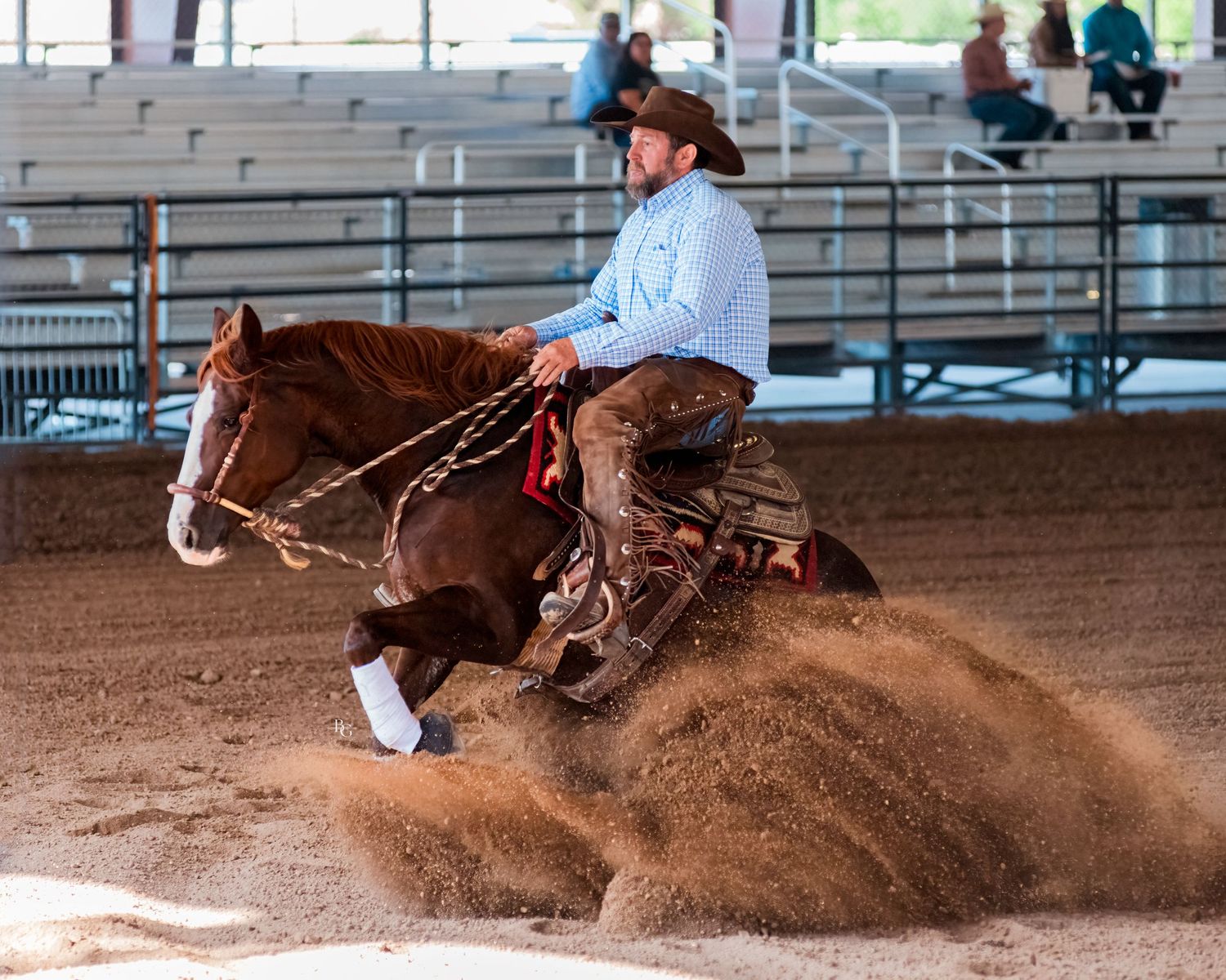 Horse and rider performing sliding stop maneuver in indoor rodeo arena.