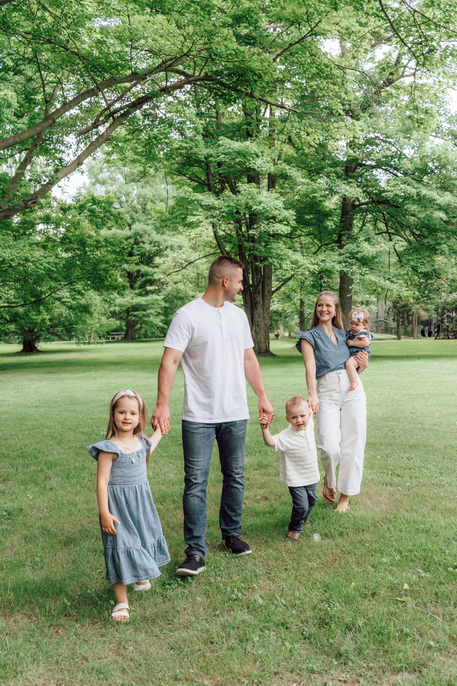 A family walking together on a lush green lawn under tall trees in a park setting. Stow, Ohio