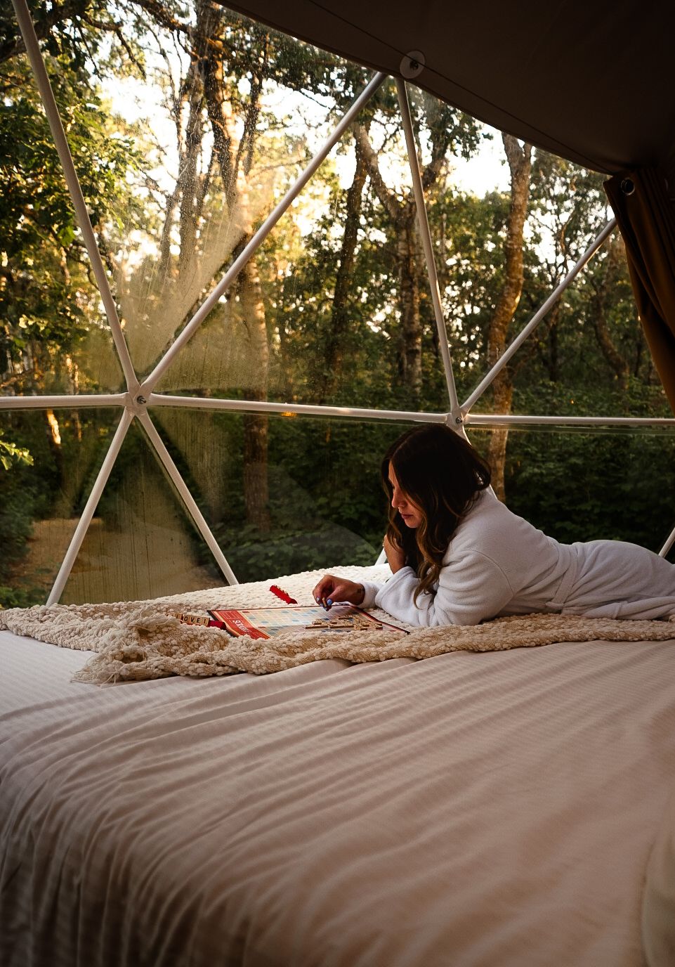 Cozy bed setup inside a glamping dome with forest views through geometric windows.