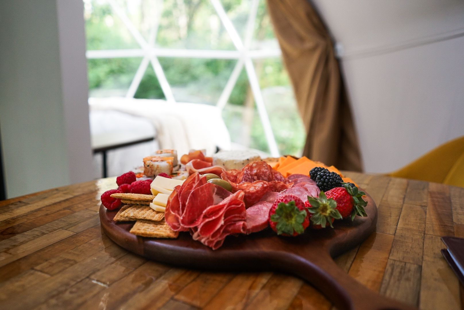 Wooden charcuterie board with meats and fresh berries served in a glamping setting.