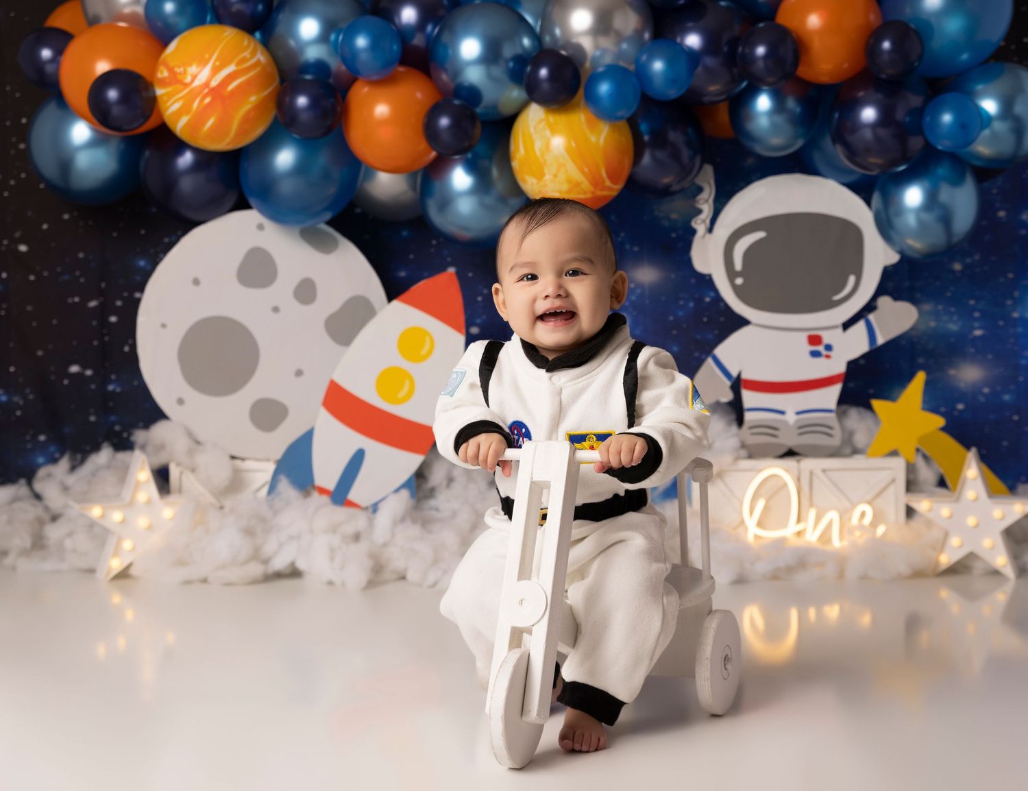 Space themed party backdrop with astronauts, planets, and blue and orange balloons.