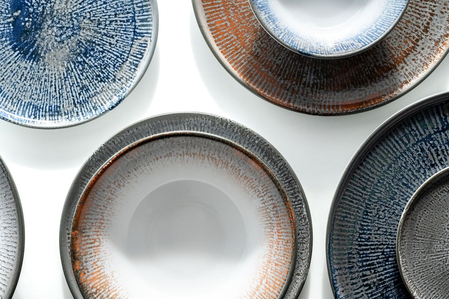 Shell collection: Porcelain plates and bowls with digitally printed radial patterns in shades of blue, brown, and grey.
