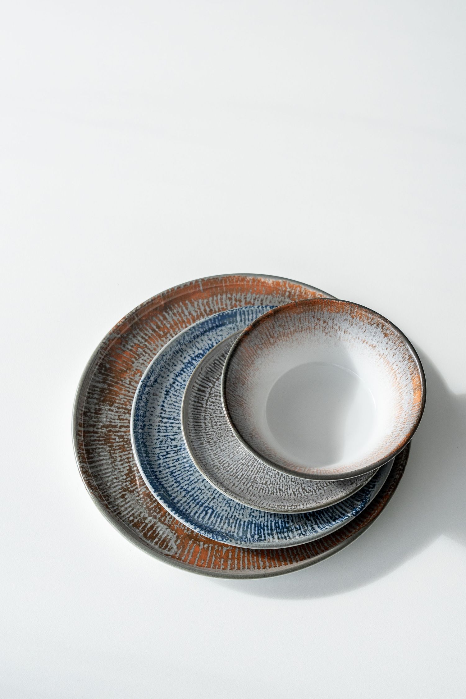 Shell collection: Porcelain plates and bowls with digitally printed radial patterns in shades of blue, brown, and grey.