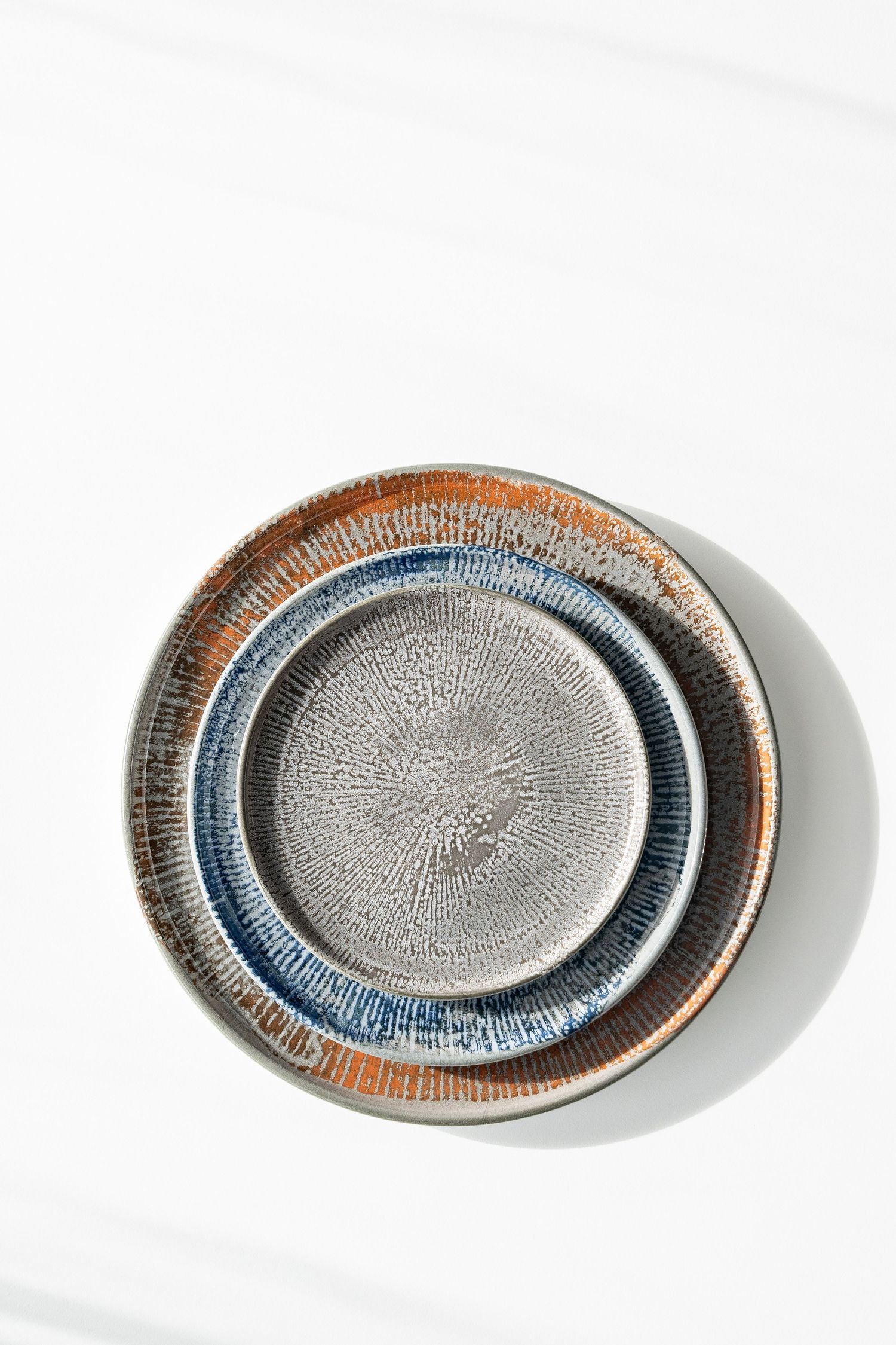 Shell collection: Porcelain plates and bowls with digitally printed radial patterns in shades of blue, brown, and grey.