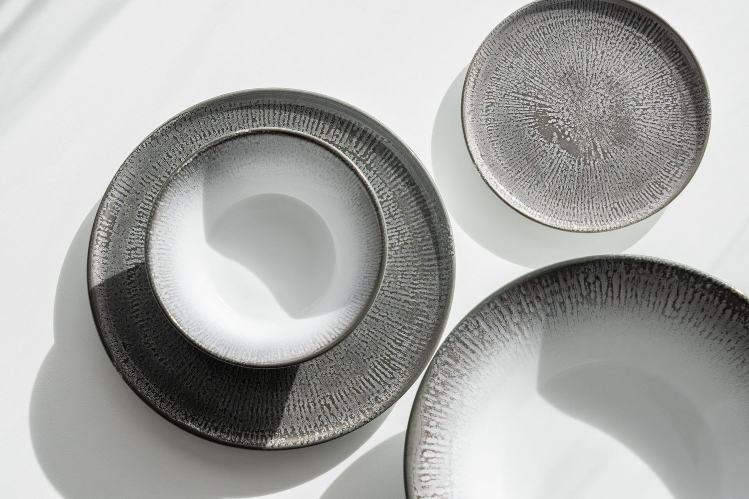 Shell collection: Porcelain plates and bowls with digitally printed radial patterns in shades of blue, brown, and grey.