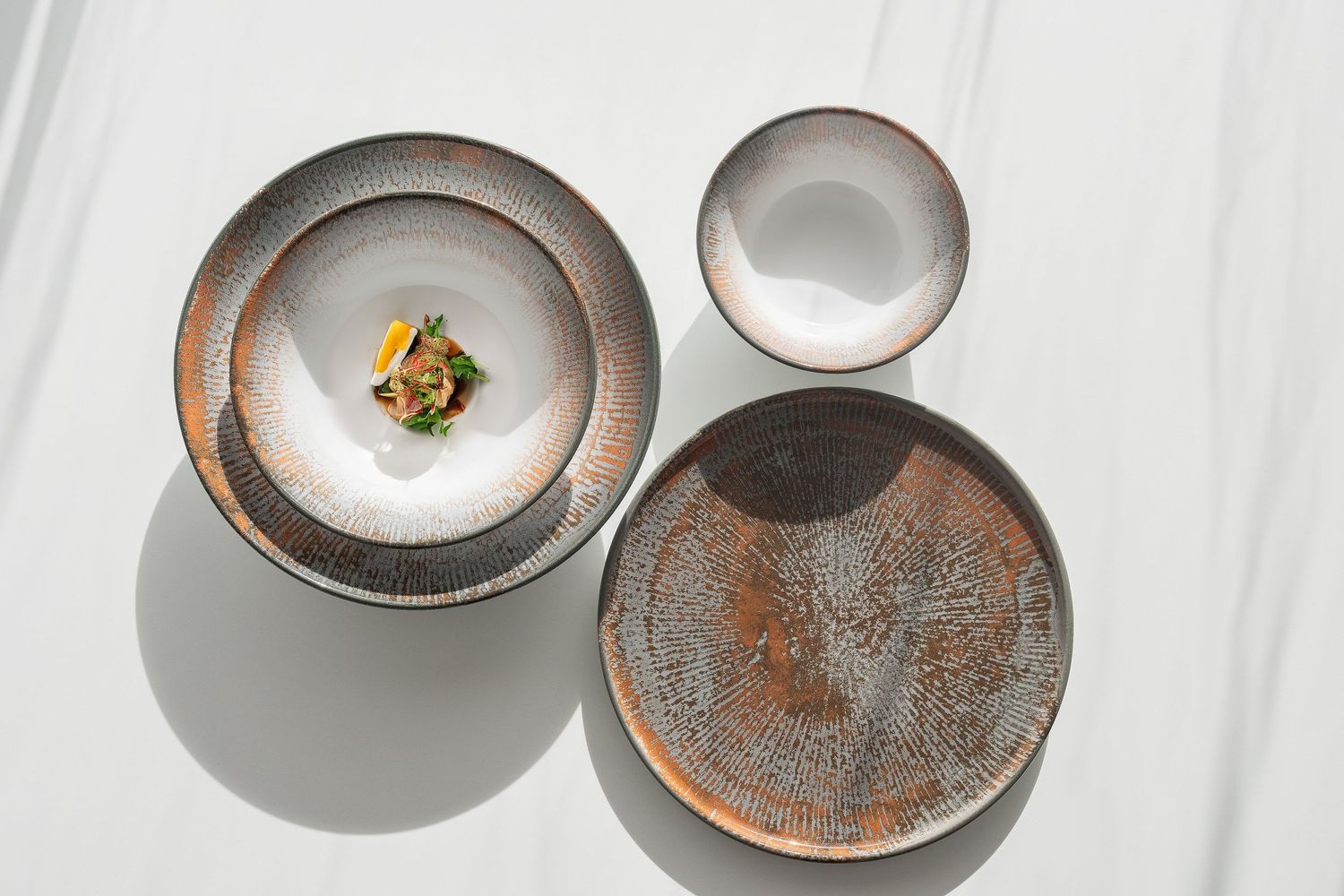 Shell collection: Porcelain plates and bowls with digitally printed radial patterns in shades of blue, brown, and grey.