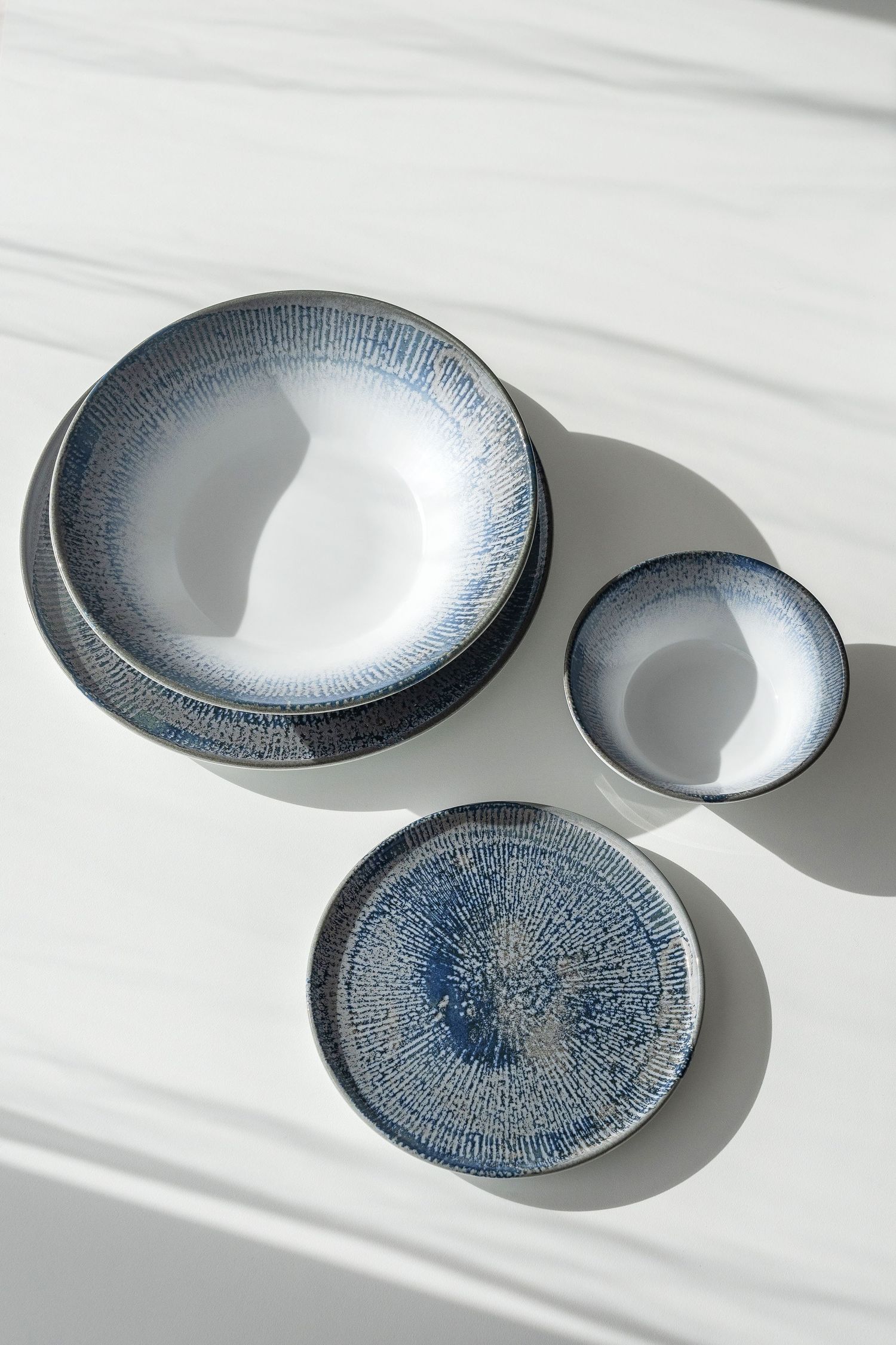 Shell collection: Porcelain plates and bowls with digitally printed radial patterns in shades of blue, brown, and grey.