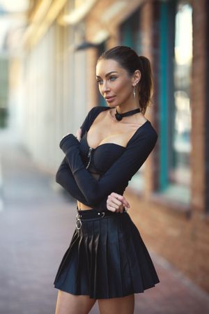 Model in black peplum dress poses on urban street with storefronts.