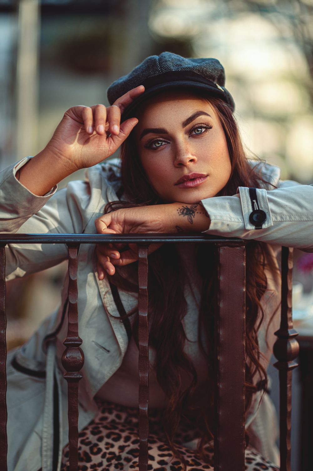 Stylish portrait featuring newsboy cap and denim jacket while leaning on railing.
