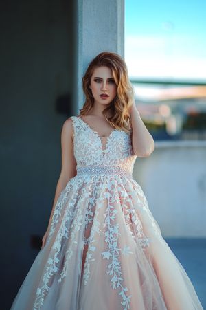 Elegant white lace wedding dress with floral appliques and empire waistline photographed against an outdoor backdrop.