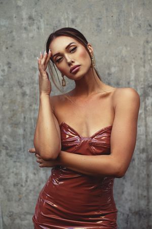 Fashion model poses in burgundy metallic dress against concrete wall.