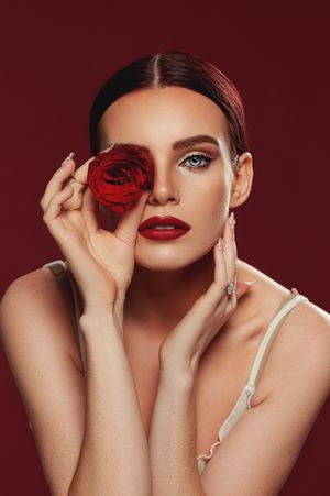 Dramatic beauty portrait with red rose and matching lipstick against burgundy background.