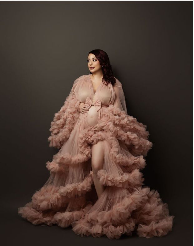 A dramatic blush pink tulle robe gown with voluminous ruffled layers photographed against a dark background.