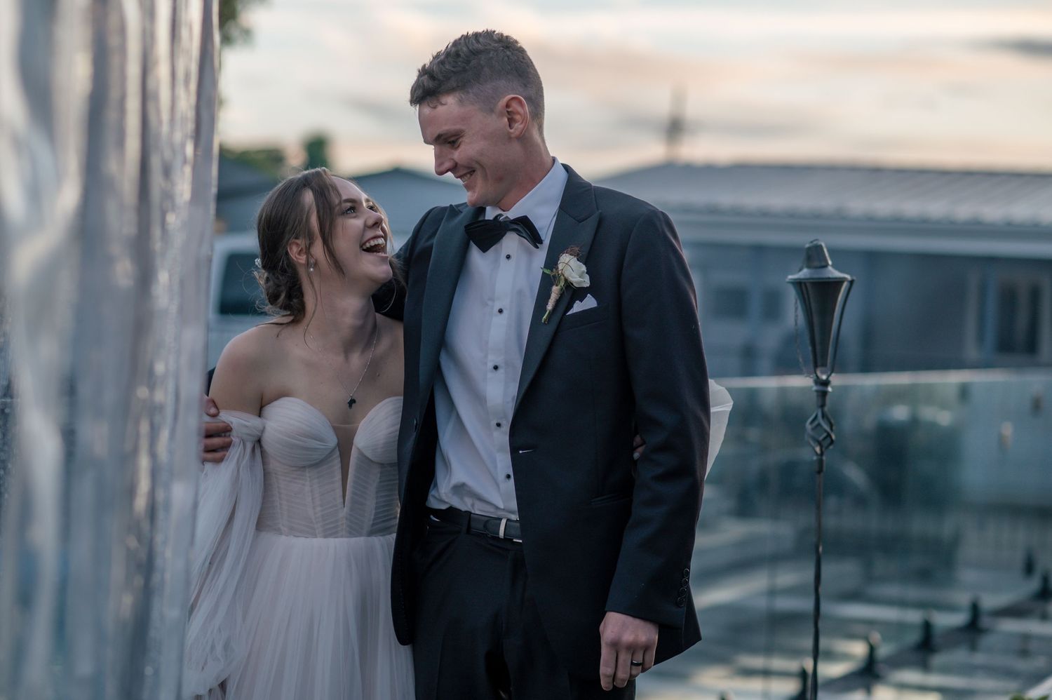 A romantic wedding couple sharing a candid moment at sunset against an urban backdrop.