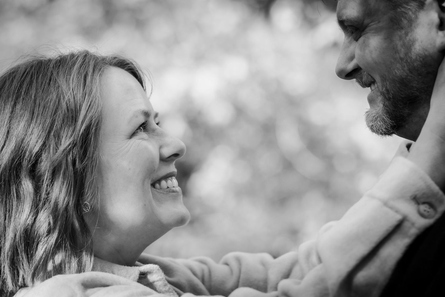 A romantic outdoor couple portrait in black and white showing tender affection against a soft bokeh background.