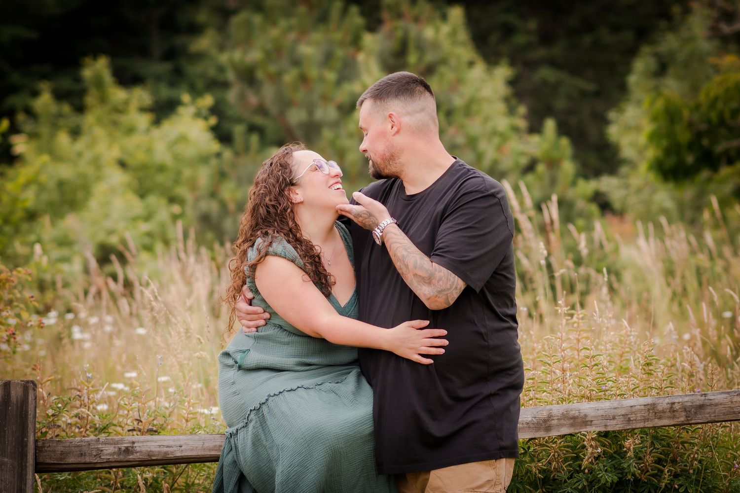Romantic couple embracing on a wooden fence in a natural outdoor setting.