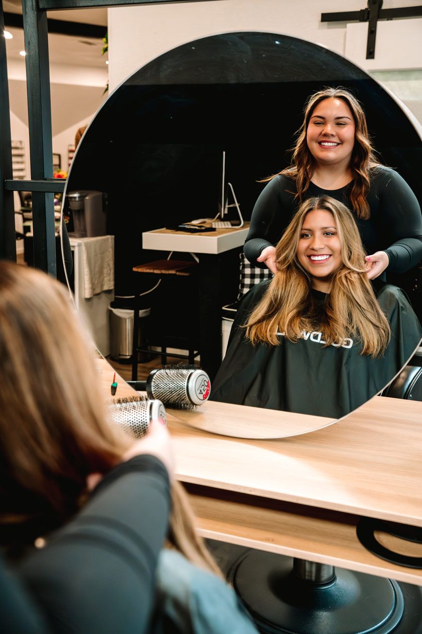 Salon mirror reflection showing styling session in progress with bright smiles.