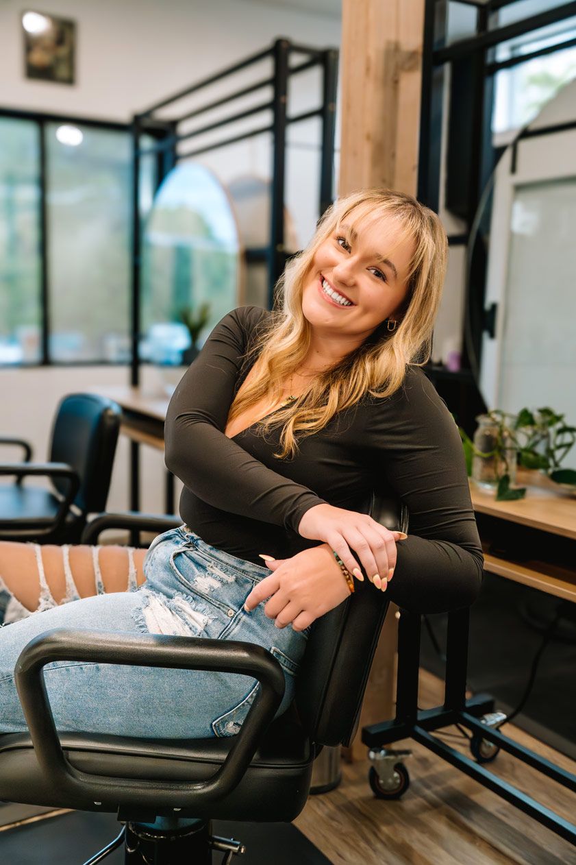 Professional sitting casually in a modern office chair wearing a black long sleeve top and distressed jeans.