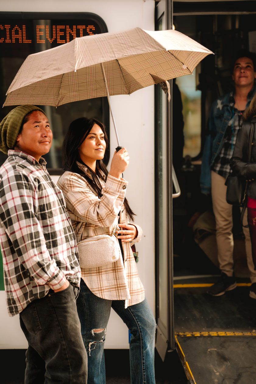 People standing under umbrellas waiting at a bus stop on a rainy day.