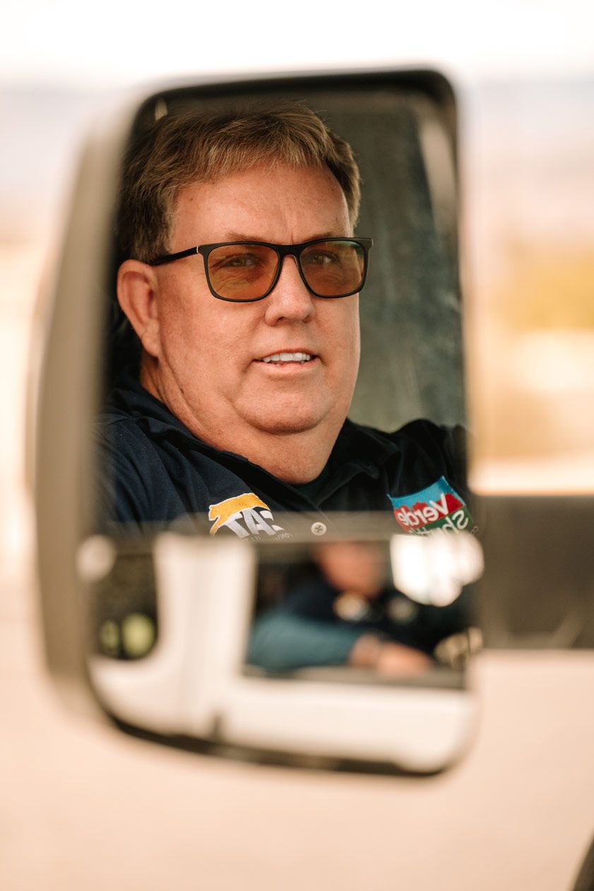 View through a side mirror of a uniformed driver in sunglasses.