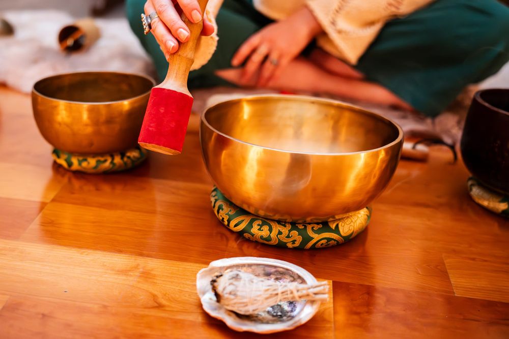 Close-up of hands playing Tibetan singing bowls on wooden surface.