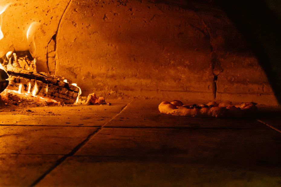 Pizza dough baking in a traditional wood-fired brick oven with flames glowing in the background.