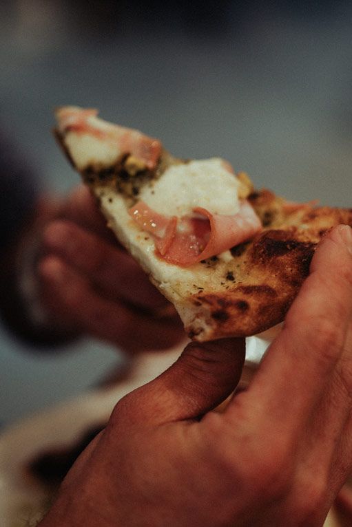 Close-up view of someone's hand holding a slice of torn pizza showing melted mozzarella cheese stretch.