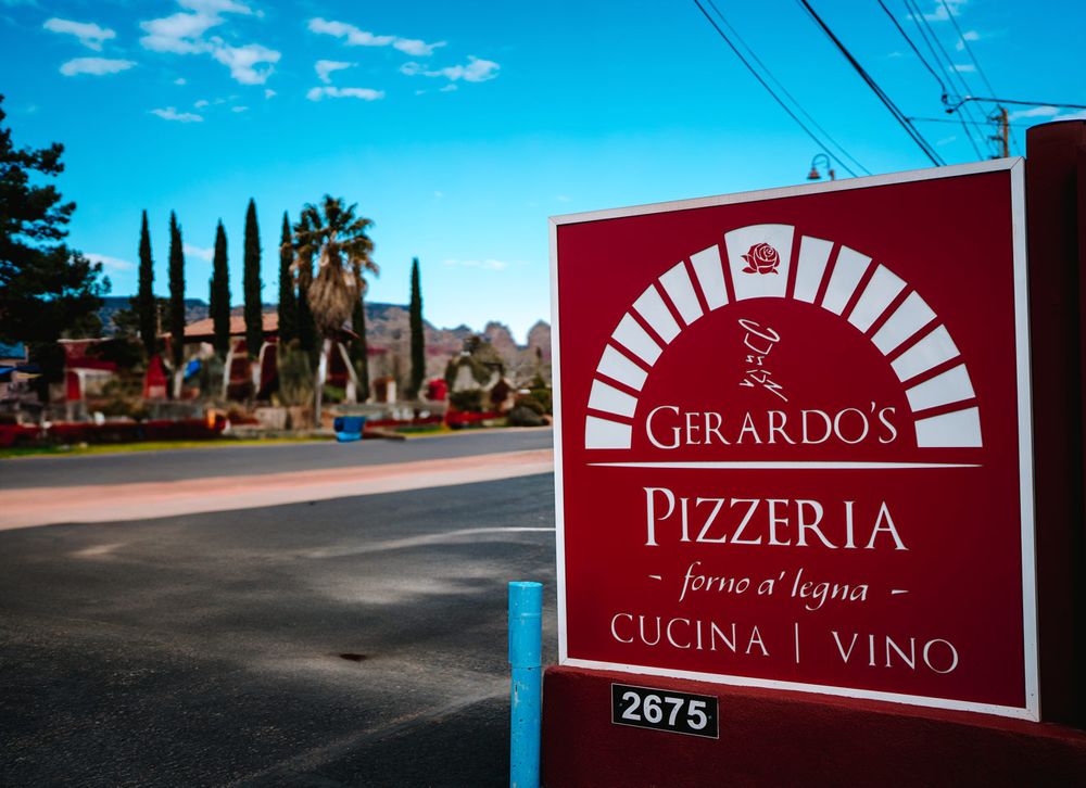 Red business sign for Gerardo's Pizzeria, in Sedona, AZ with Italian cypress trees and palm trees visible against blue sky.
