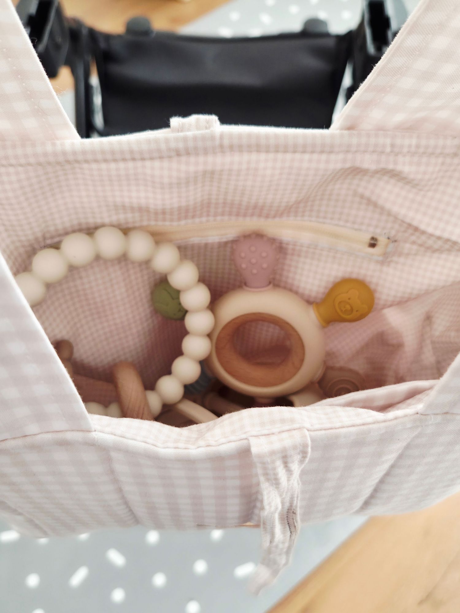 Pink gingham diaper bag with baby teething toys, silicone beaded bracelet, and wooden rattles inside.