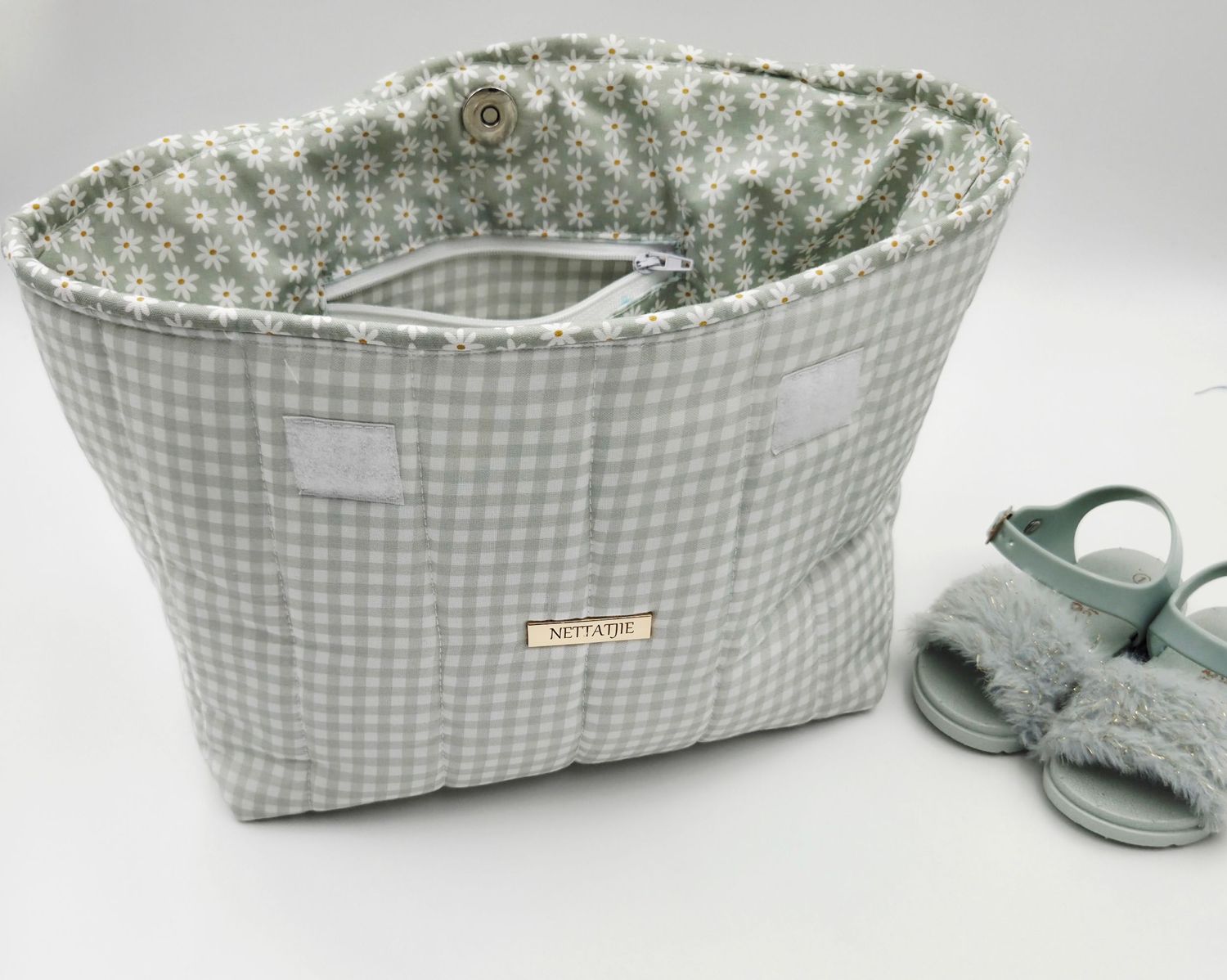 Gray gingham fabric tote bag with floral lining and zipper closure, displayed next to matching sage green sandals.