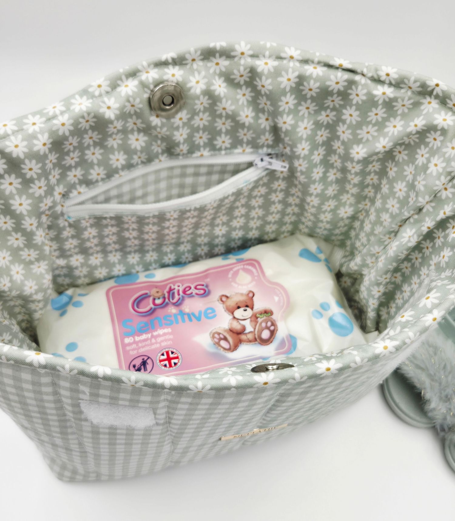 Gray floral diaper bag interior with Cuties Sensitive diapers pack and white wipes inside.