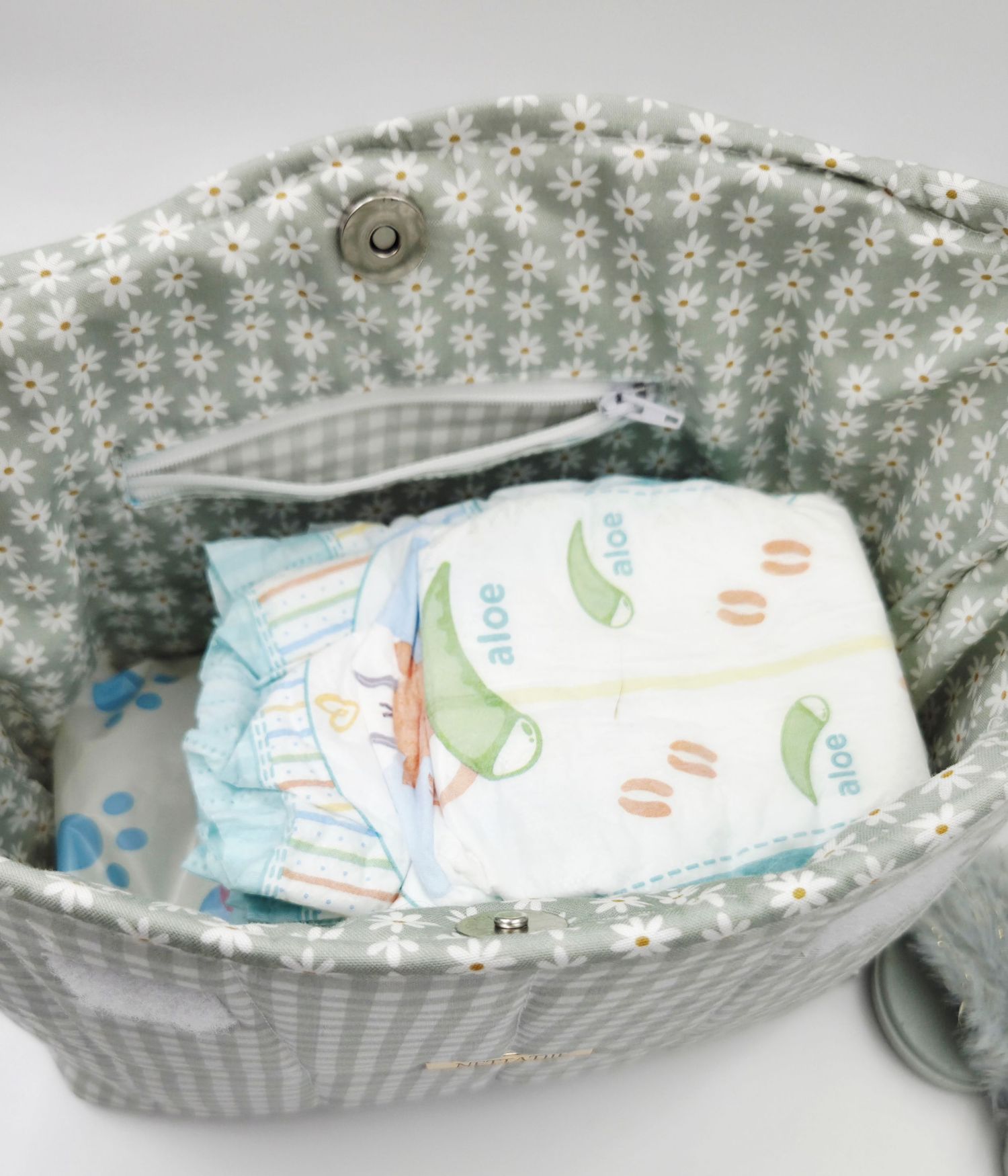 Gray gingham diaper bag open showing neatly stacked baby diapers with daisy floral lining interior.