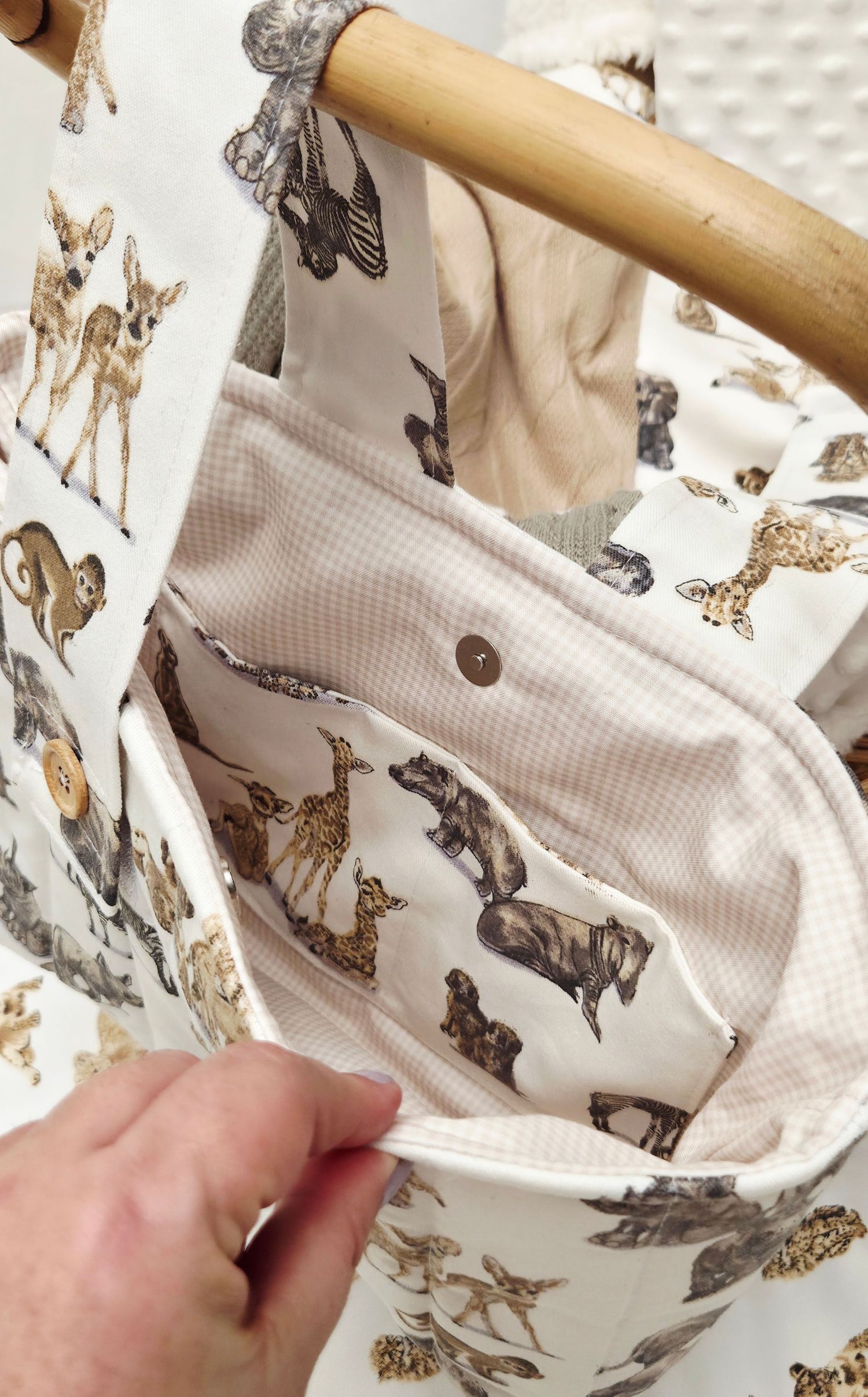 Interior view of a fabric tote bag with woodland animal print lining, featuring a snap pocket and wooden handle.