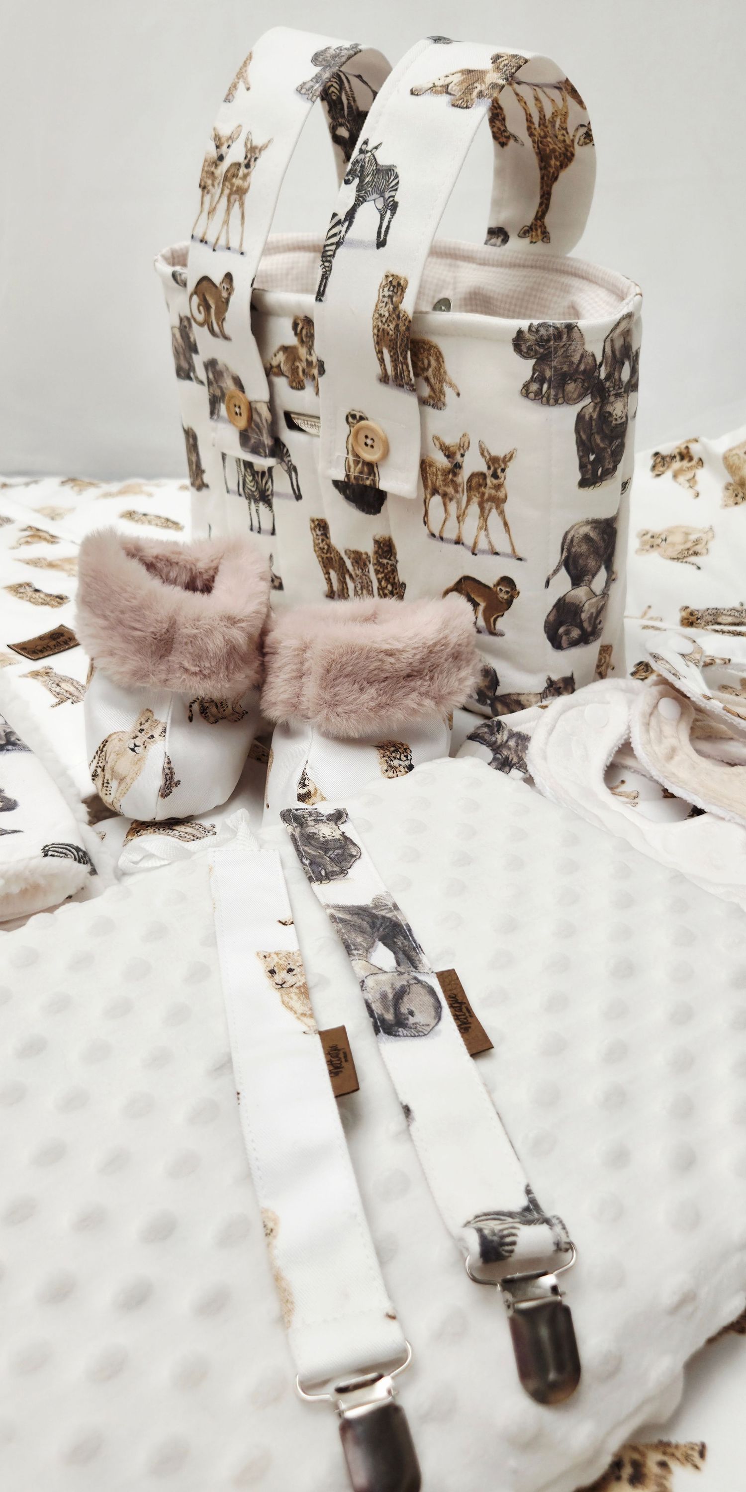 Baby gift set with animal print backpack, booties, suspenders, and blanket in neutral tones.