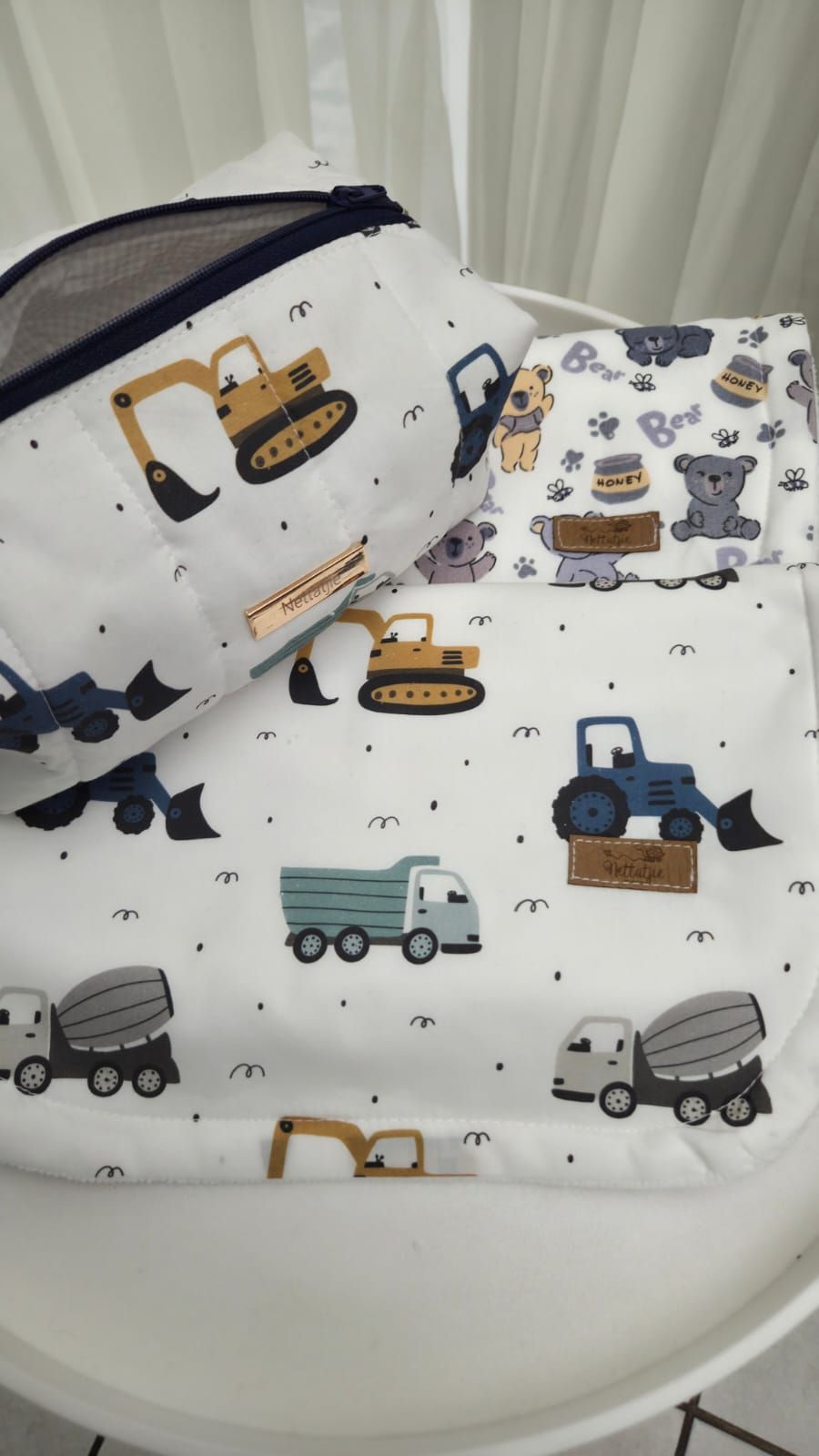 White baby bedding set featuring colorful construction vehicles and teddy bear patterns, displayed in a bassinet.