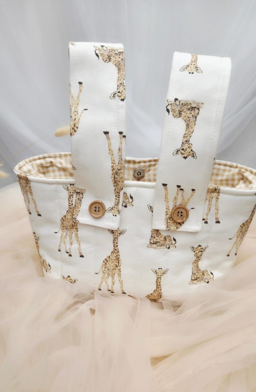 White fabric tote bag and straps featuring giraffe print pattern with tan gingham lining and wooden button accents.