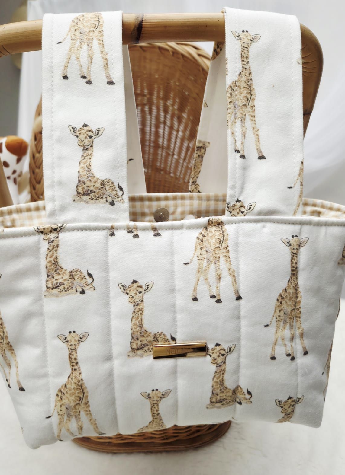 White quilted tote bag featuring adorable baby giraffe print pattern, displayed in a wicker basket.