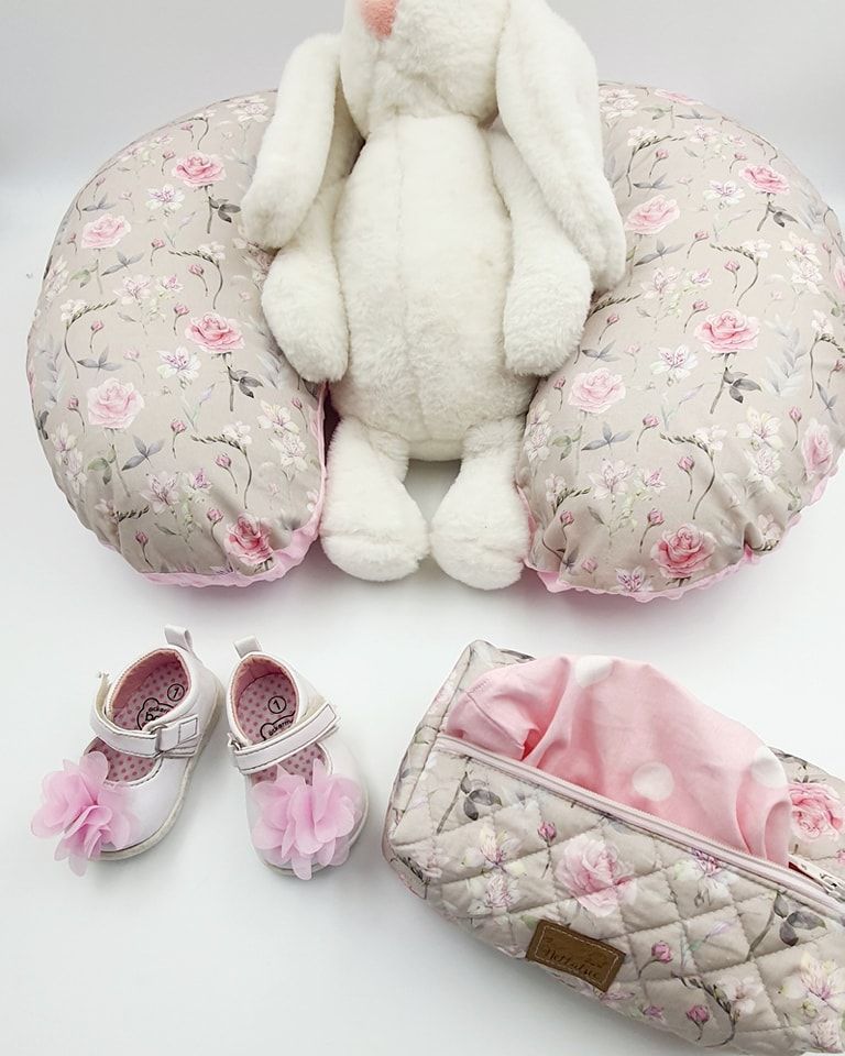 Plush white bunny with floral print nursing pillow and baby accessories arranged on white surface.