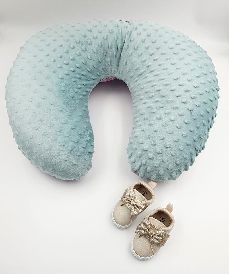 Mint green minky nursing pillow with textured dots and small beige baby shoes.