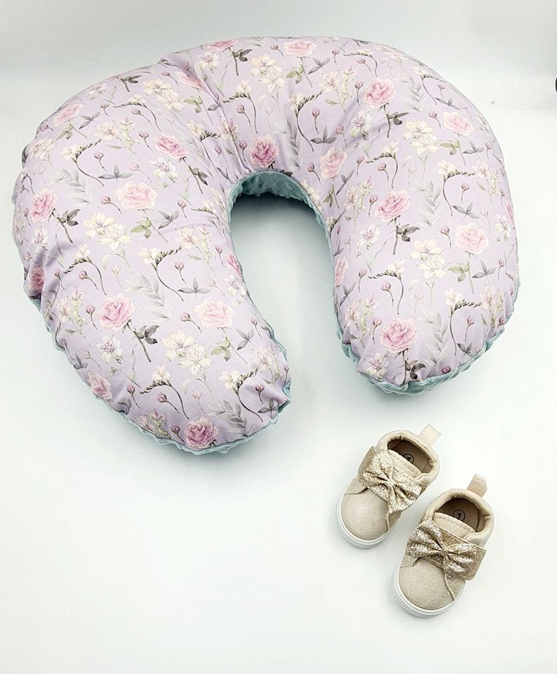 Curved nursing pillow with delicate pink floral pattern and beige bow shoes.