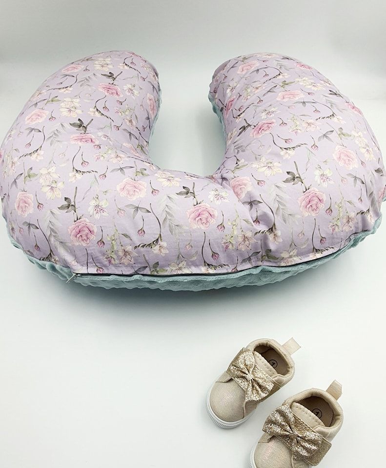 U-shaped nursing pillow with romantic rose print and decorative baby shoes.