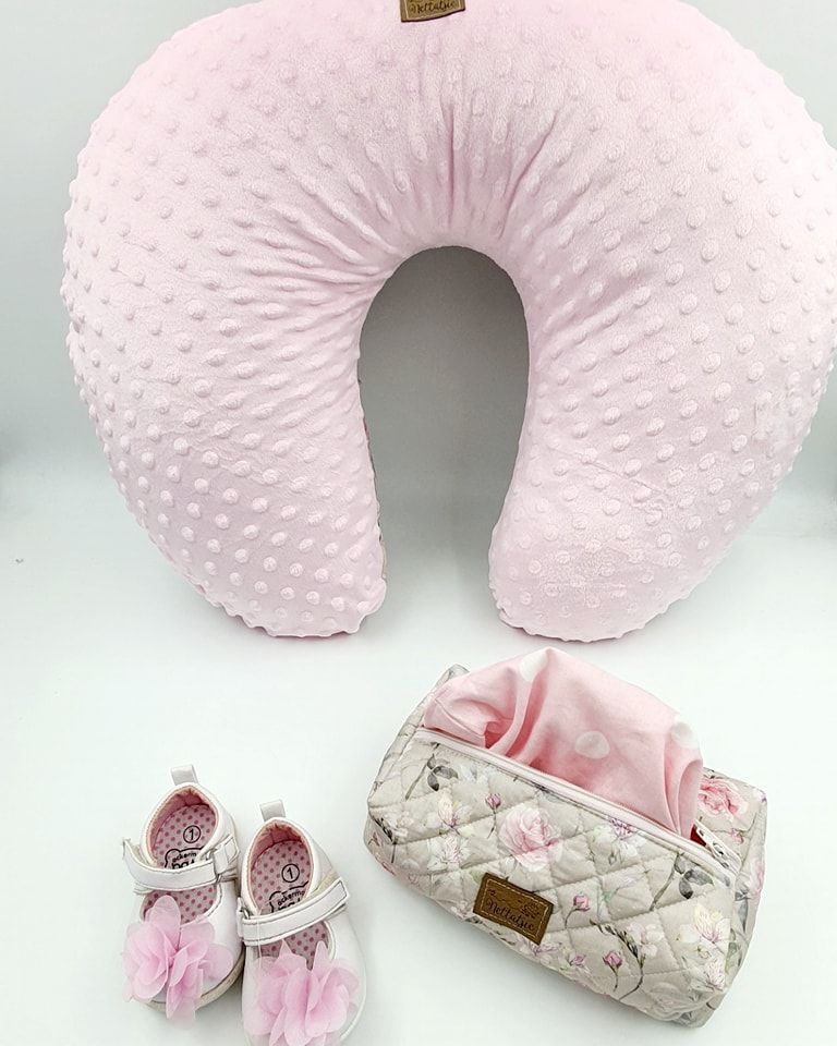 Pink minky nursing pillow with floral accessories and tiny decorative shoes.