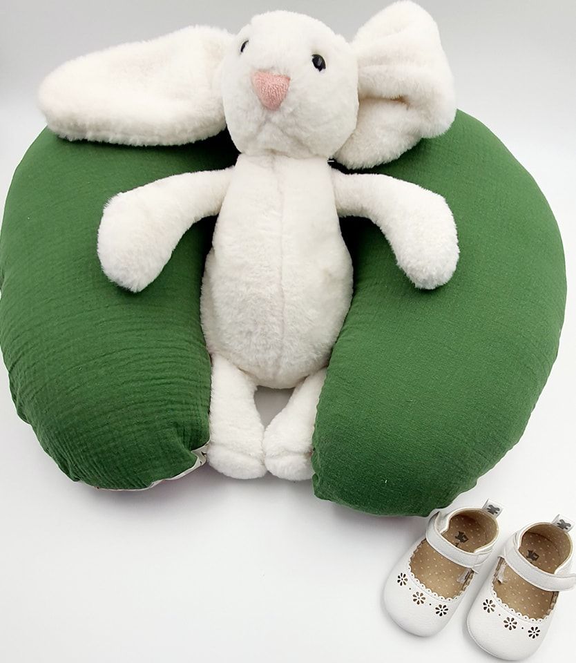 White plush bunny on green nursing pillow with infant shoes.