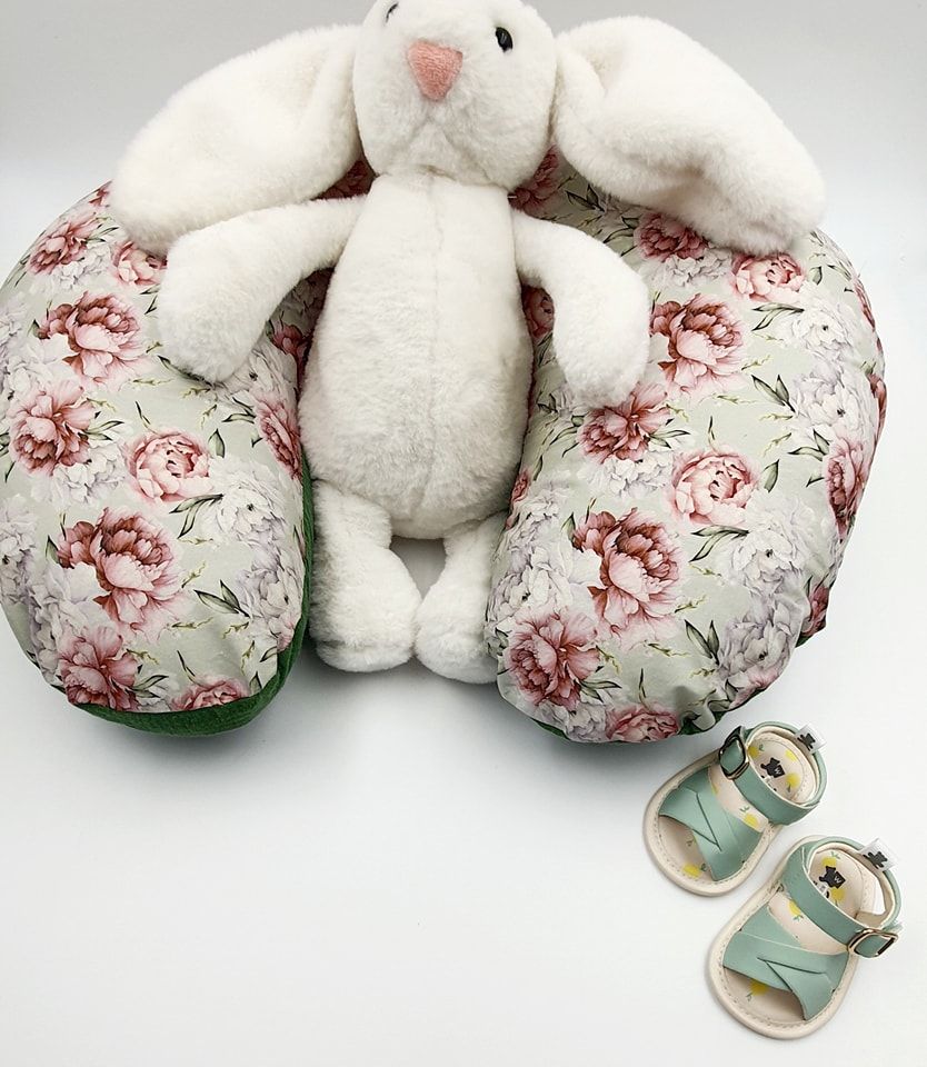 White plush nursing pillow with floral pattern and matching baby shoes.