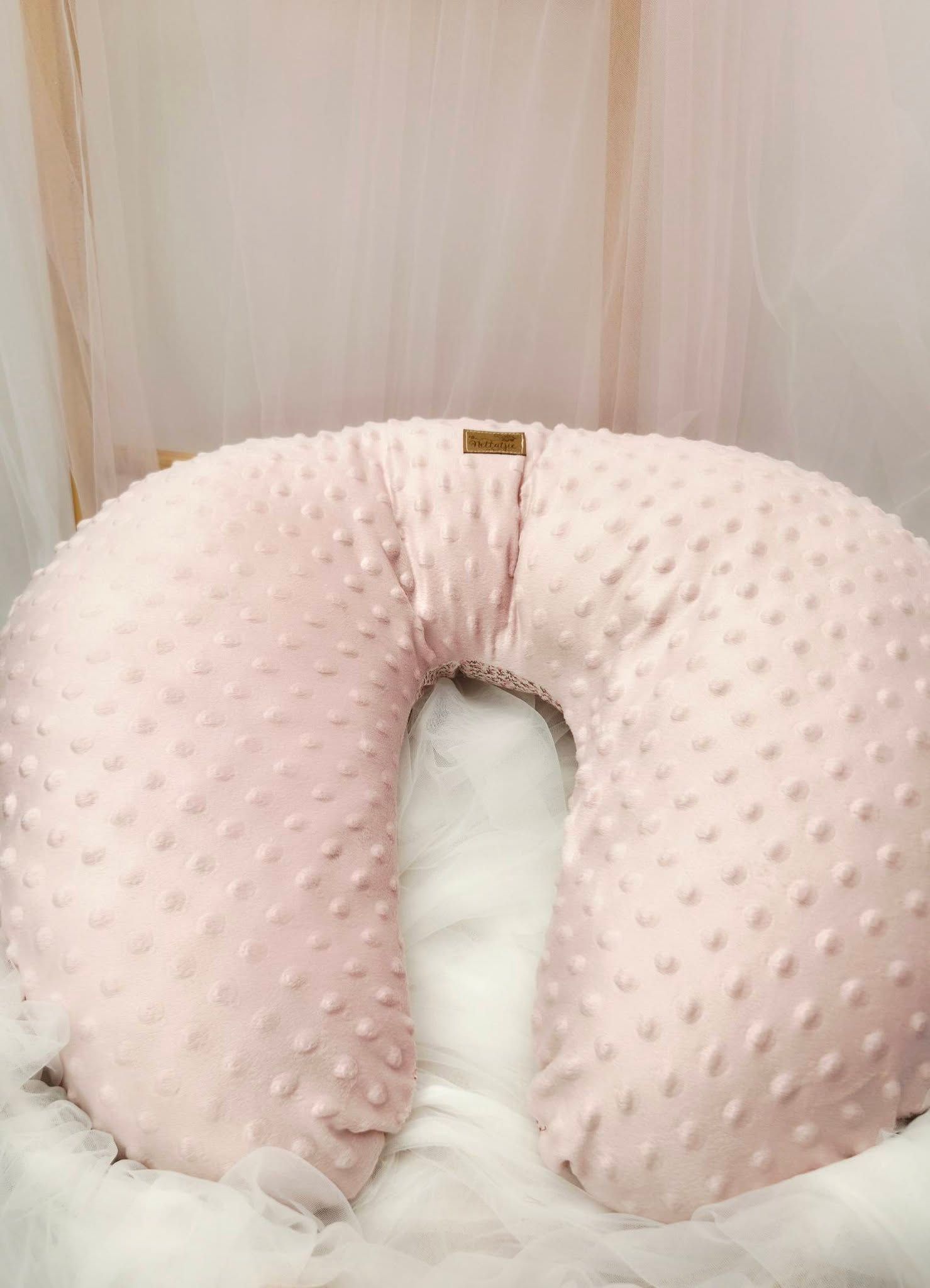 Pink minky dot nursing pillow with textured bubble fabric, displayed in a soft white nursery setting.