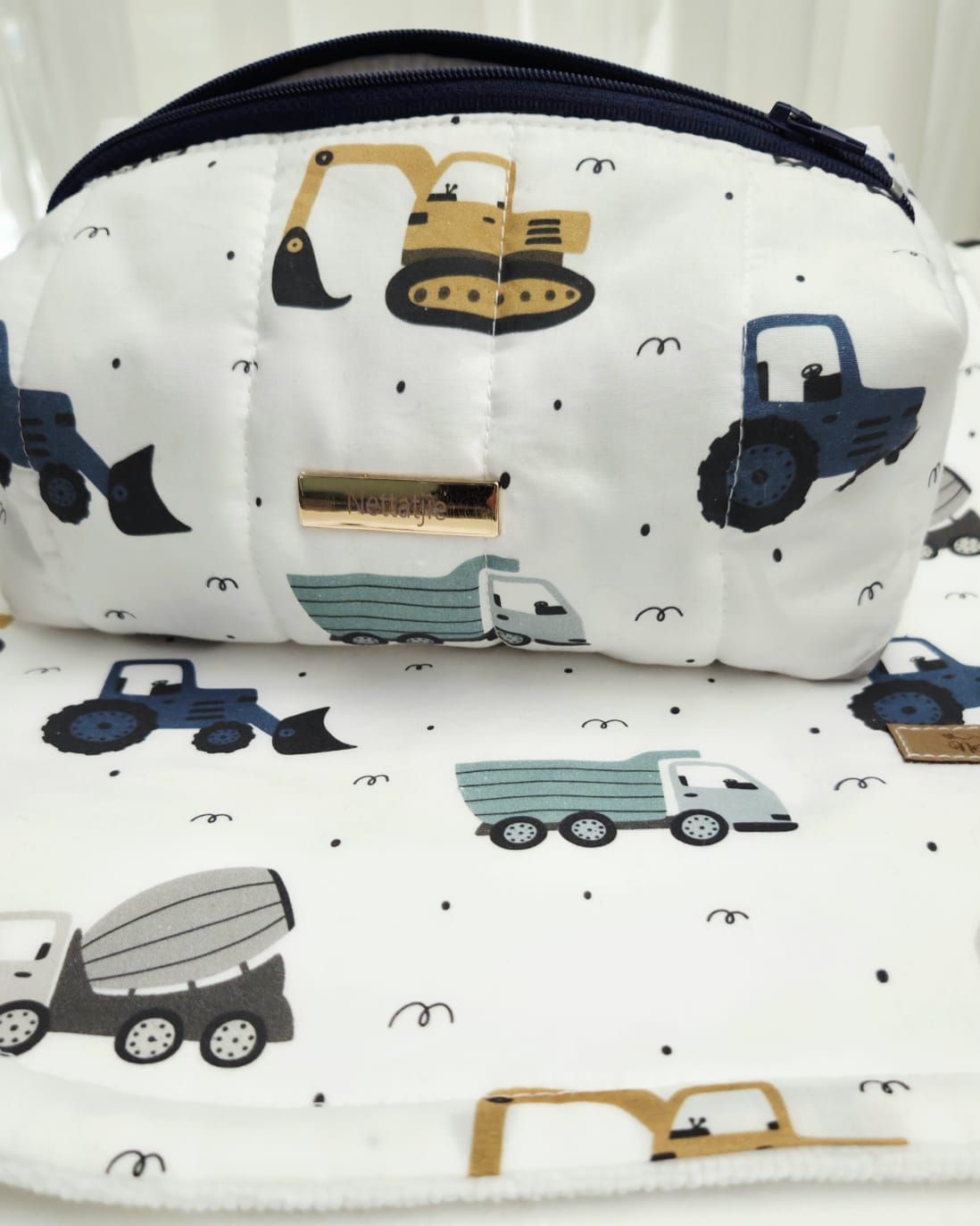 White kids fabric pouch with construction vehicles pattern featuring tractors, dump trucks, and excavators in navy, teal, and gold.